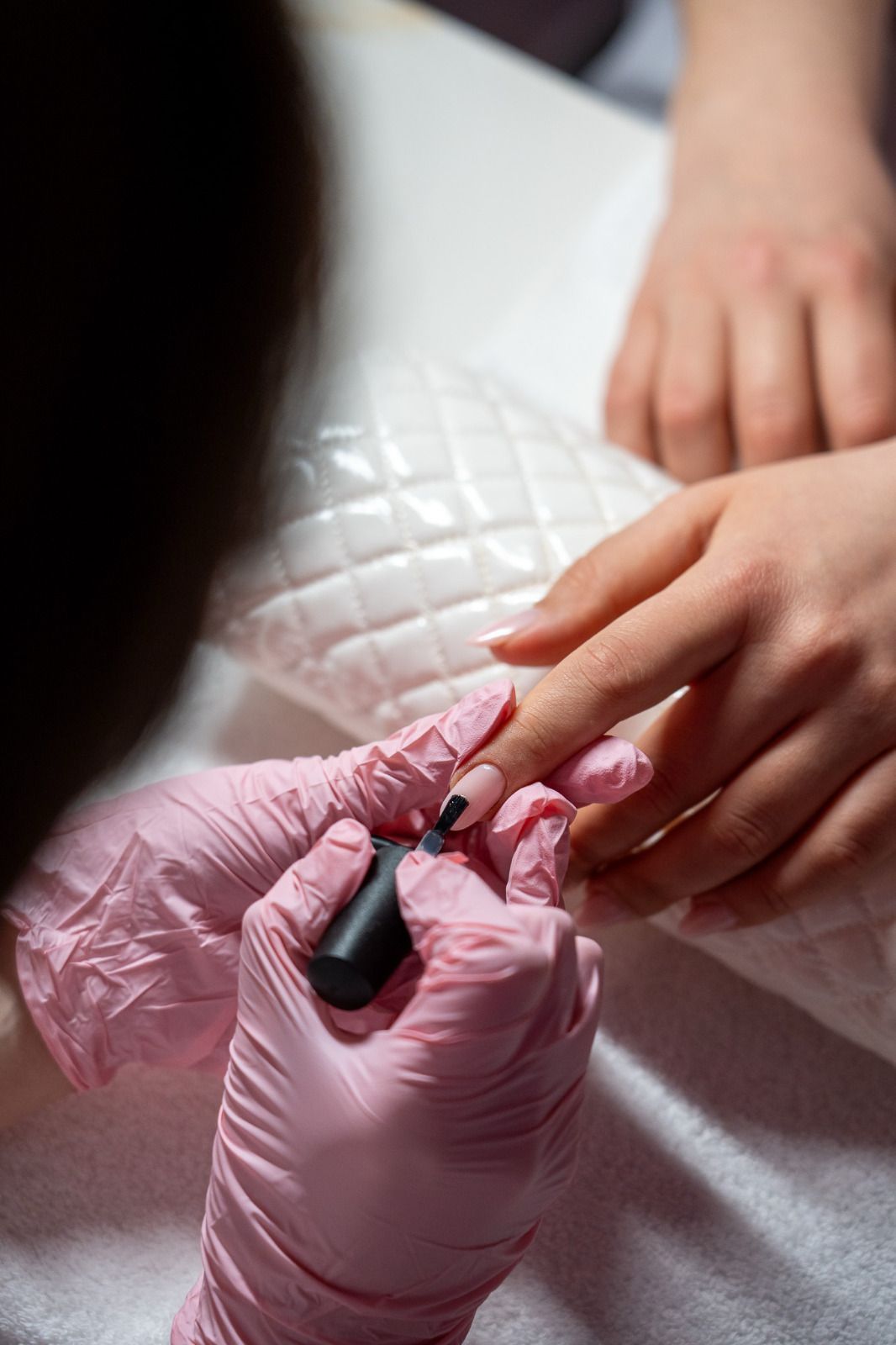 Una donna si fa dipingere le unghie da una nail artist che indossa guanti rosa.