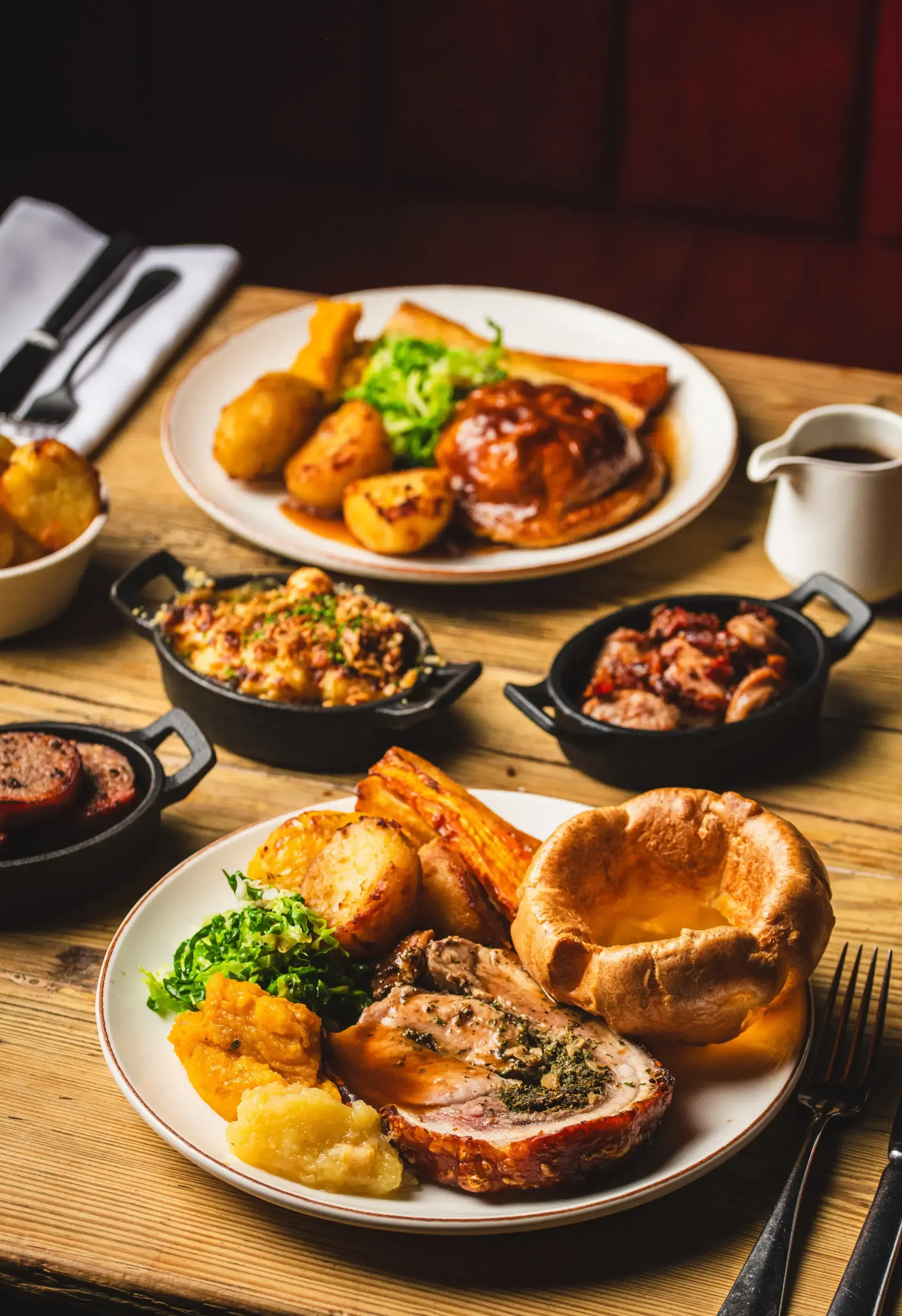 The Queens Head, Dorking | Plates of roasted meat, vegetables, and gravy on a wooden table, in a restaurant setting.