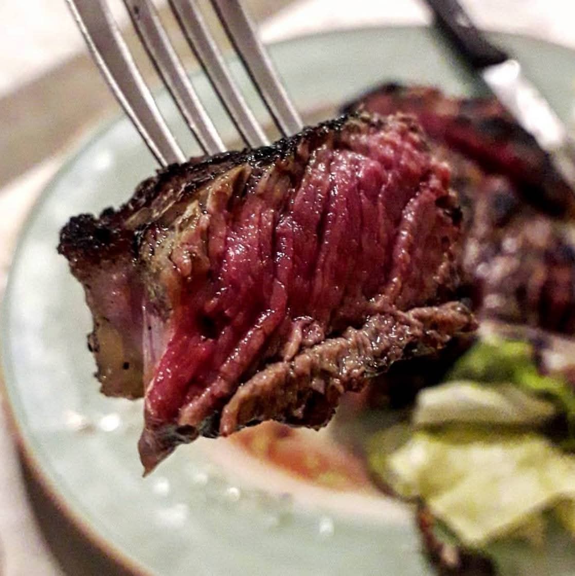 Forchetta che regge una fetta di bistecca al sangue con il centro rosa su un piatto con verdure