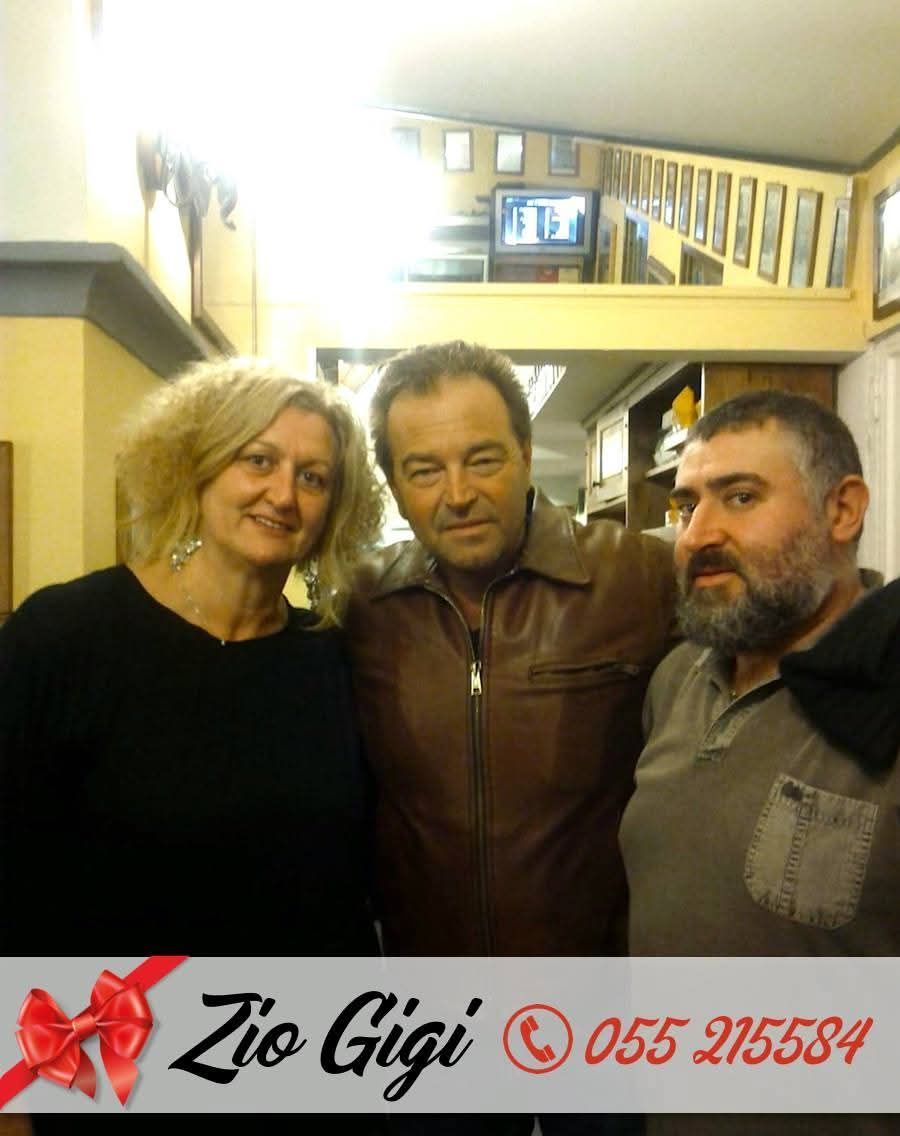 Tre persone in posa all'interno di un locale, vicino all'insegna e al bancone di un ristorante, sorridono all'obiettivo.
