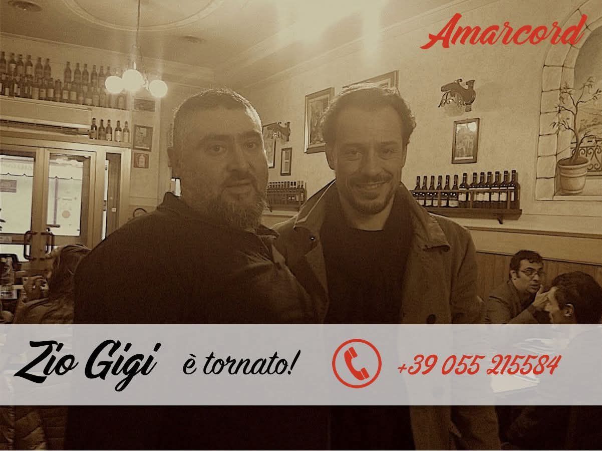 Due uomini sorridenti in un bar illuminato da una luce calda, con la scritta “Zio Gigì è tornato!” e uno striscione con un numero di telefono.