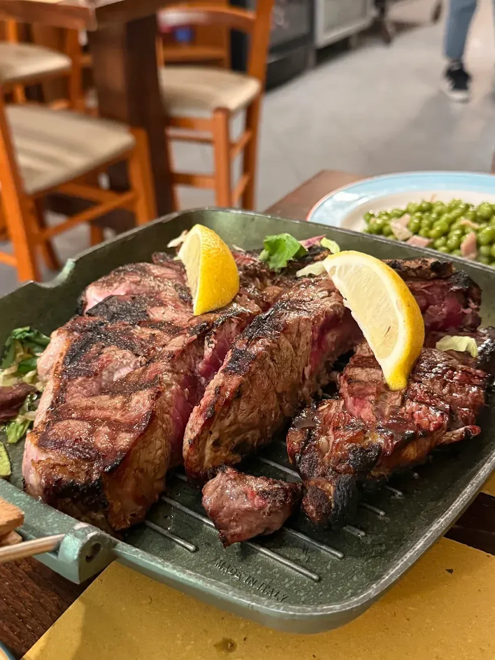 Piatto di bistecca alla griglia con spicchi di limone su un piatto verde in un ambiente da ristorante.