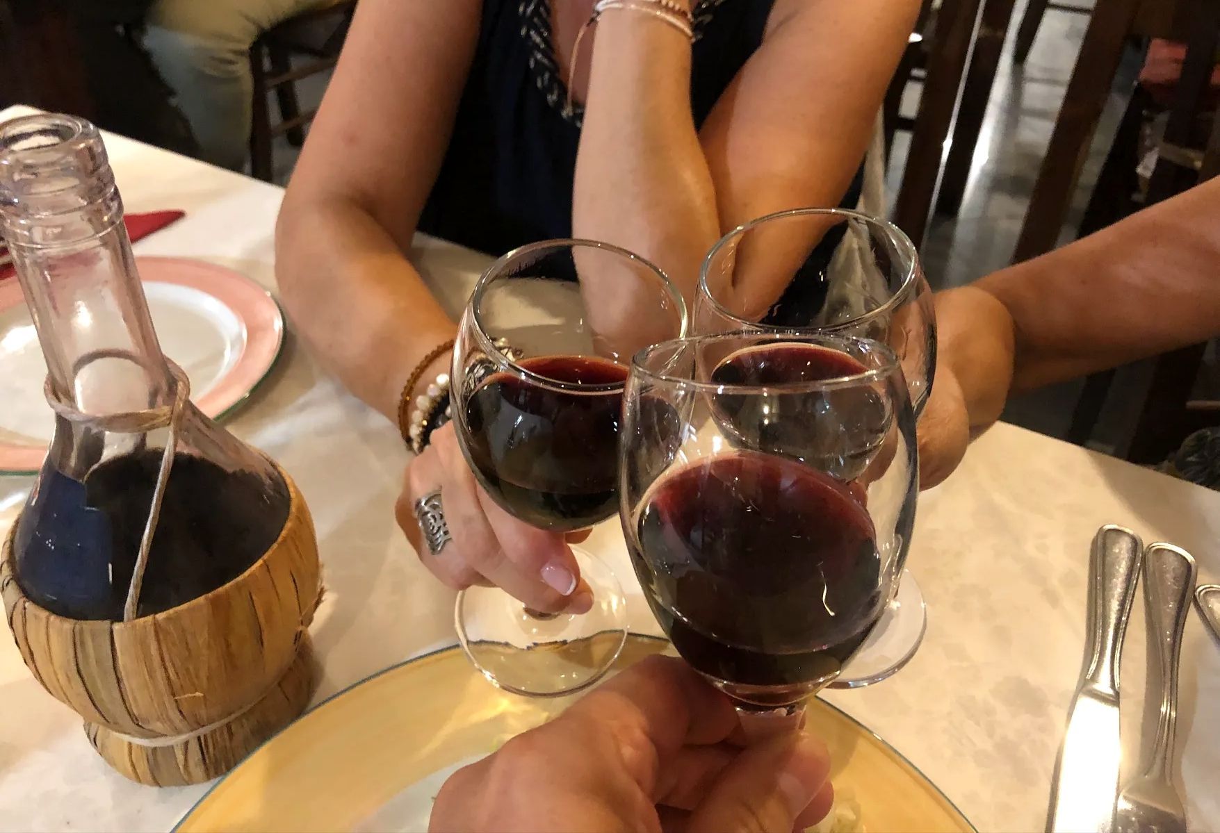 Tre persone brindano con calici di vino rosso a un tavolo di un ristorante.
