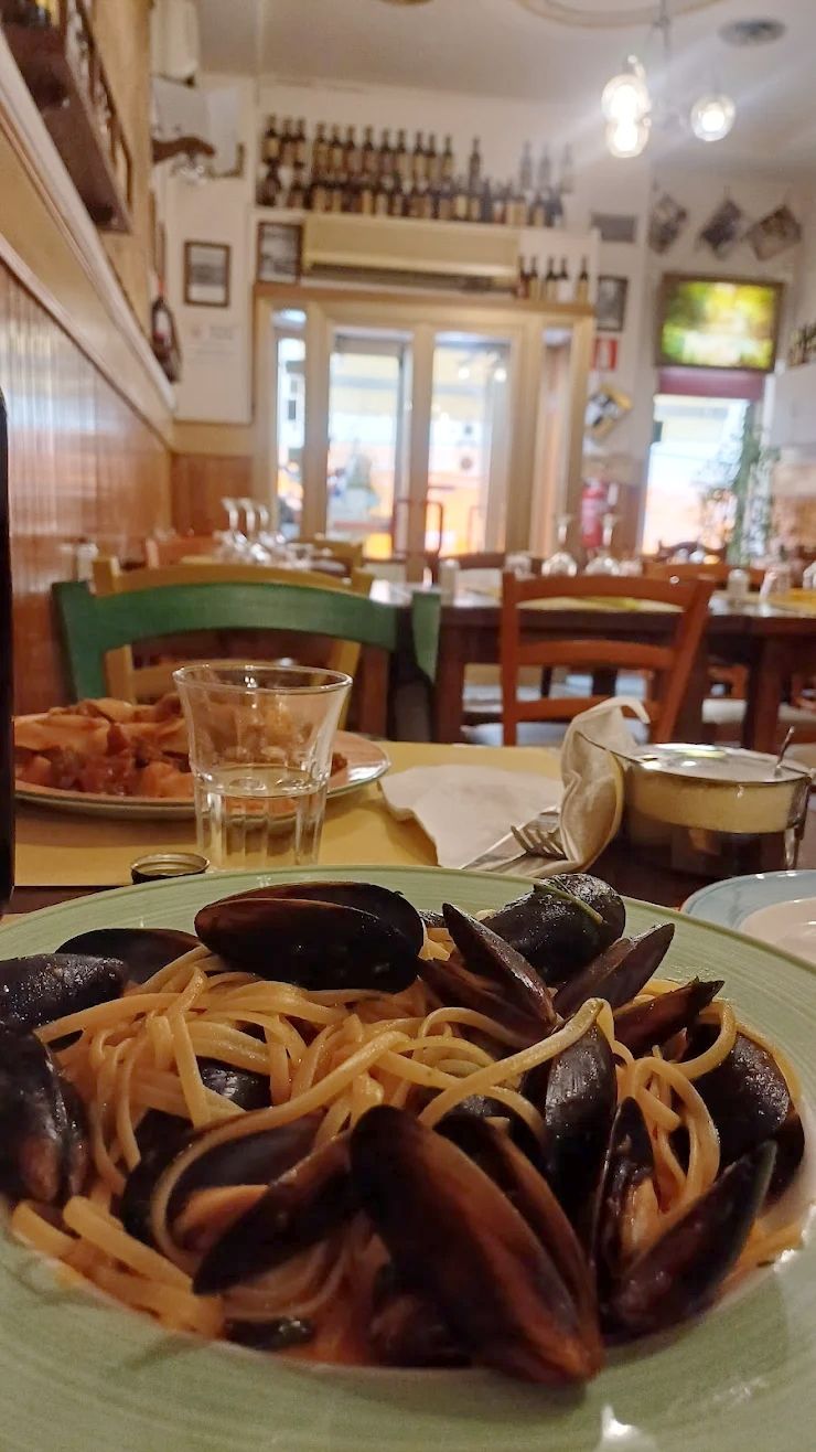 Un piatto di pasta su un tavolo in un accogliente ristorante, con bevande e sedie sullo sfondo.