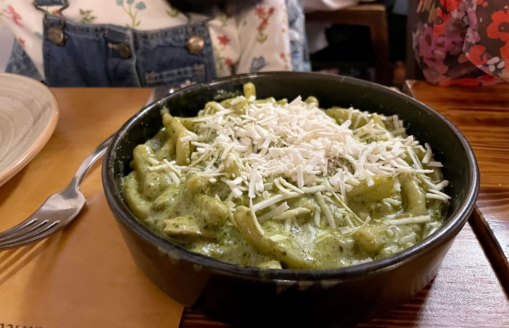 Una ciotola di pasta verde condita con formaggio grattugiato su un tavolo di ristorante.