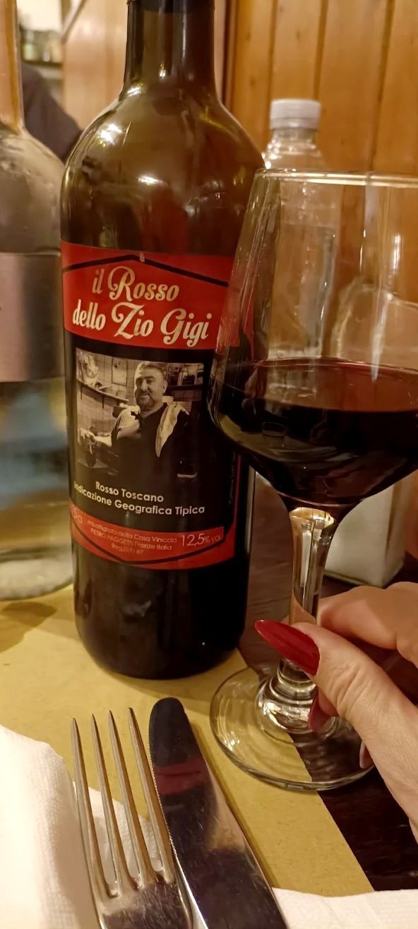 Una bottiglia di vino e un bicchiere pieno su un tavolo di un ristorante, accanto a una candela accesa e alle posate.