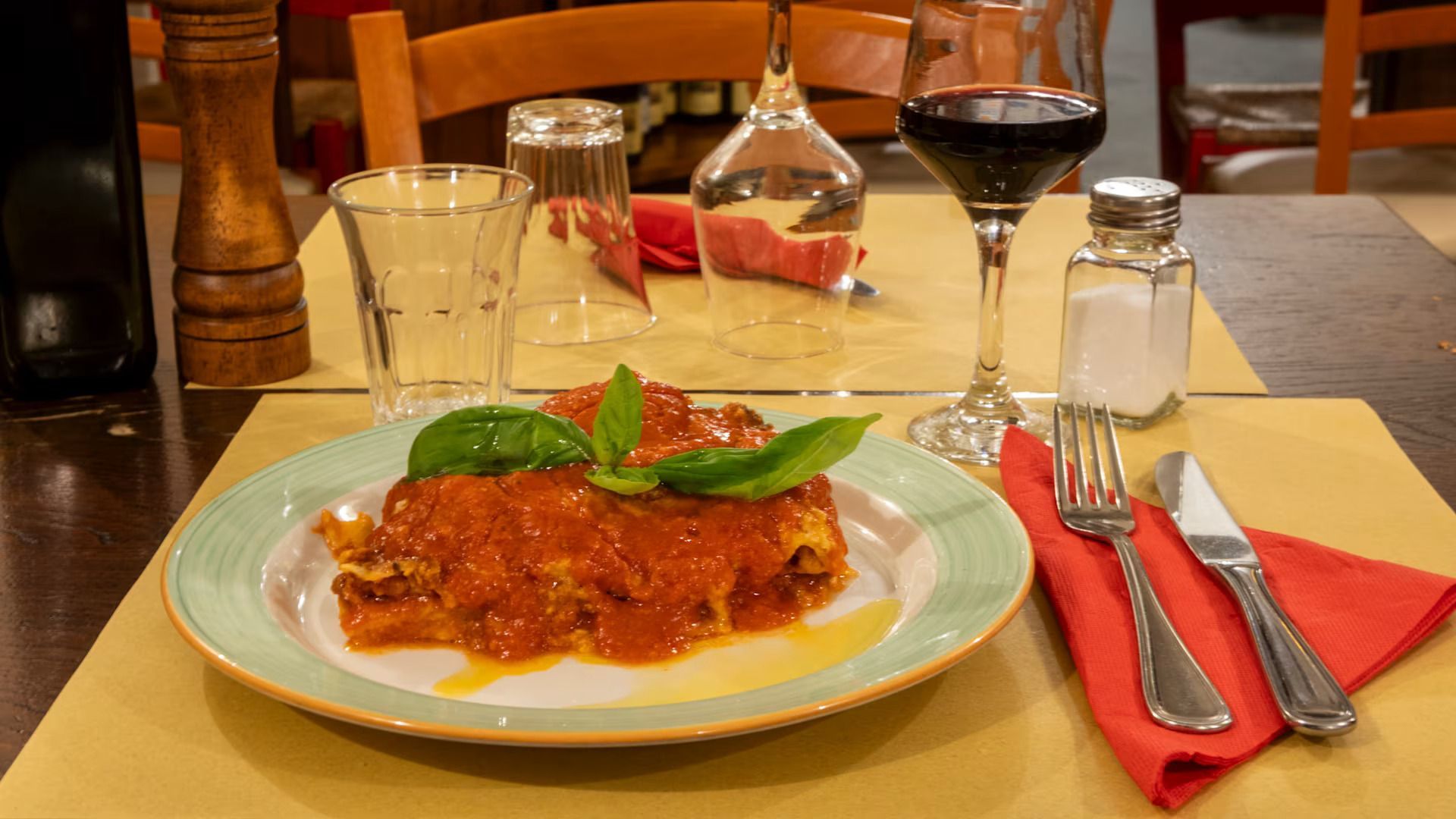 Piatto di pasta al sugo di pomodoro e basilico su un tavolo da ristorante con bicchieri da vino e posate.