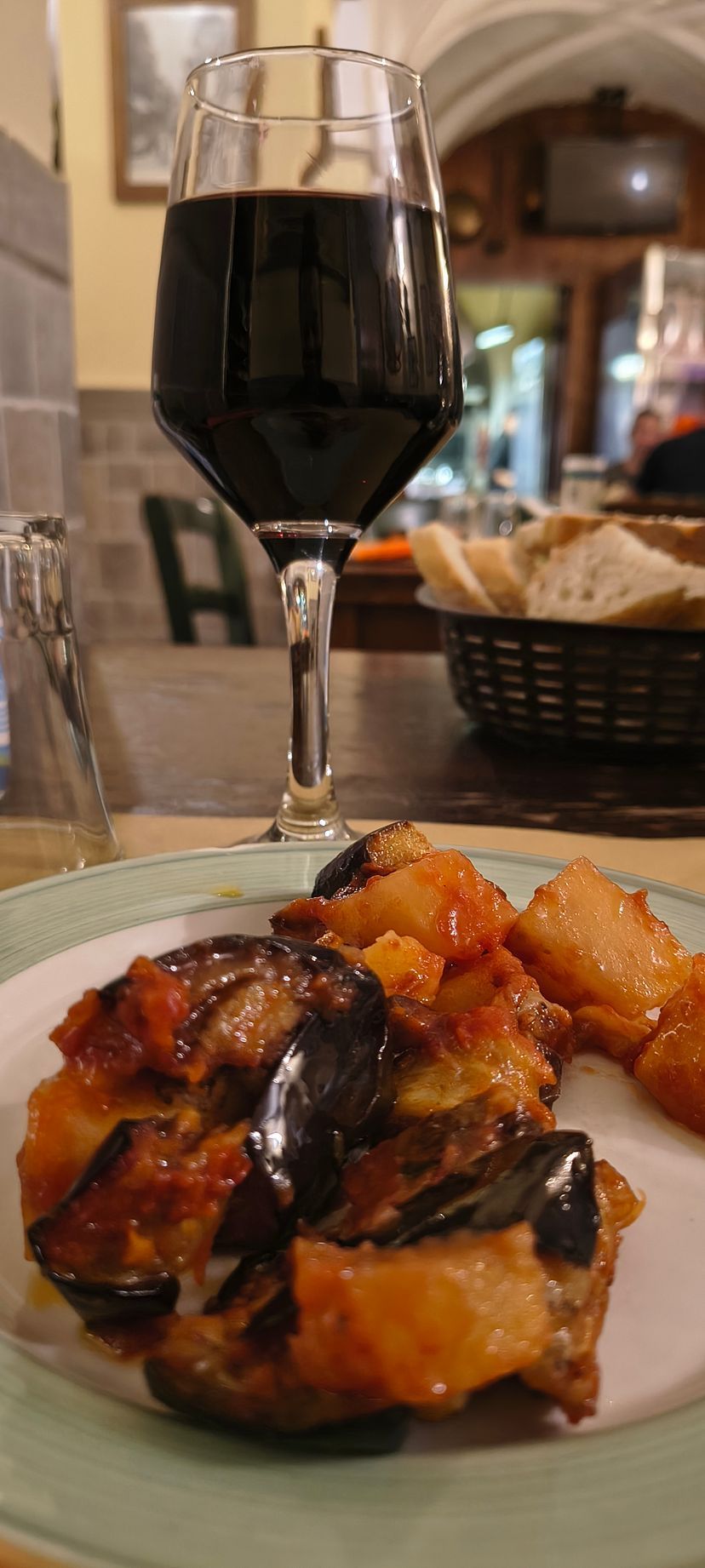 Un calice di vino e un piatto di cibo arrosto su un tavolo in un ristorante illuminato da luci soffuse.
