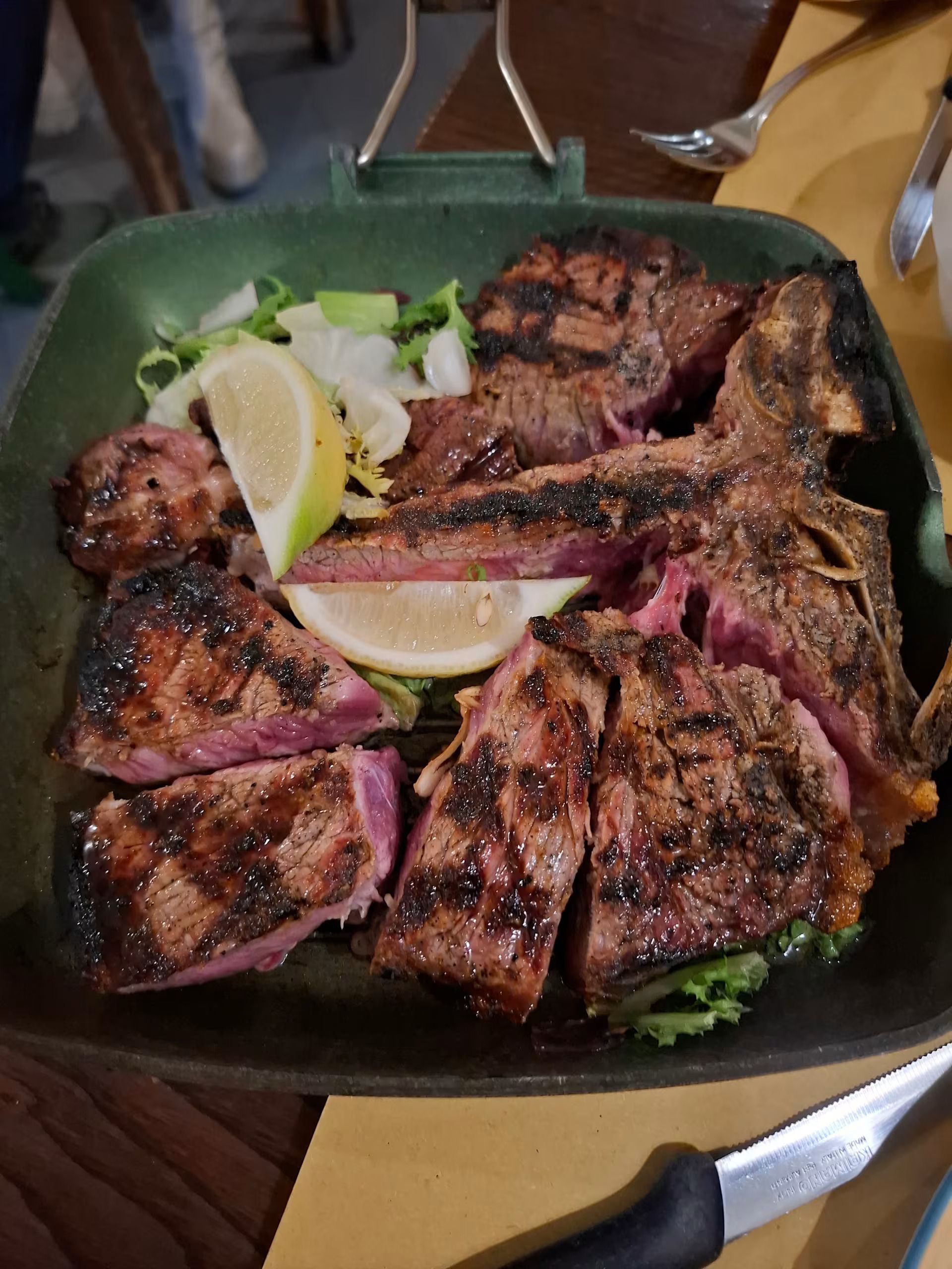 Carne grigliata a fette su un piatto con spicchi di limone e verdure, servita su un tavolo