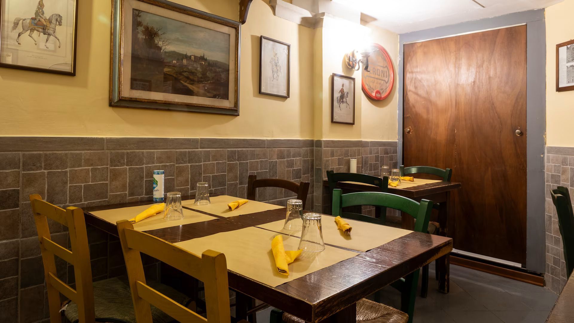 Accogliente sala da pranzo del ristorante con tavoli e sedie in legno, quadri incorniciati e una grande porta in legno.