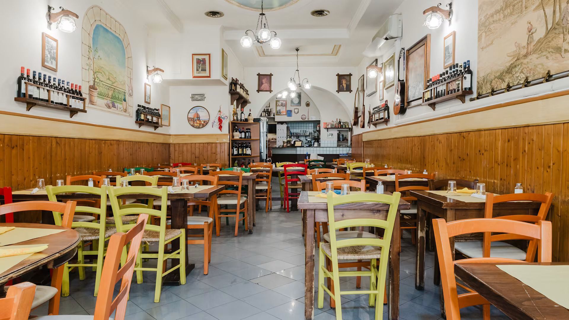Interno vuoto e accogliente di un ristorante con tavoli in legno, sedie colorate e opere d'arte alle pareti.
