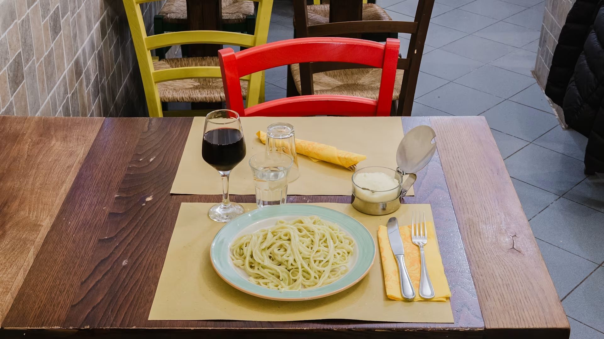 Un piatto di pasta servito su un tavolo di legno con un bicchiere di vino, pane e posate in un caffè.