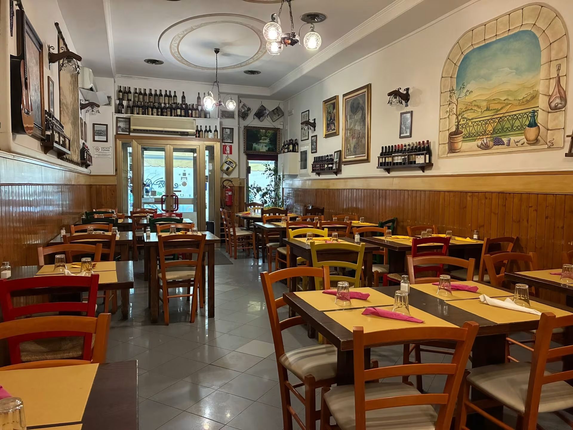 Accogliente sala da pranzo del ristorante con tavoli e sedie in legno, opere d'arte alle pareti e una luminosa porta sul retro.