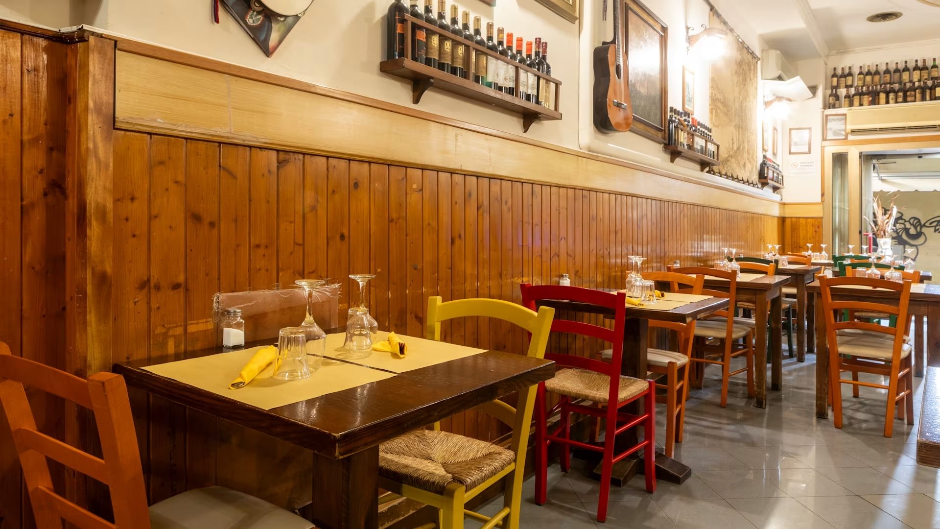 Ristorante rustico vuoto con tavoli, sedie e decorazioni alle pareti in legno lungo una stretta sala da pranzo.