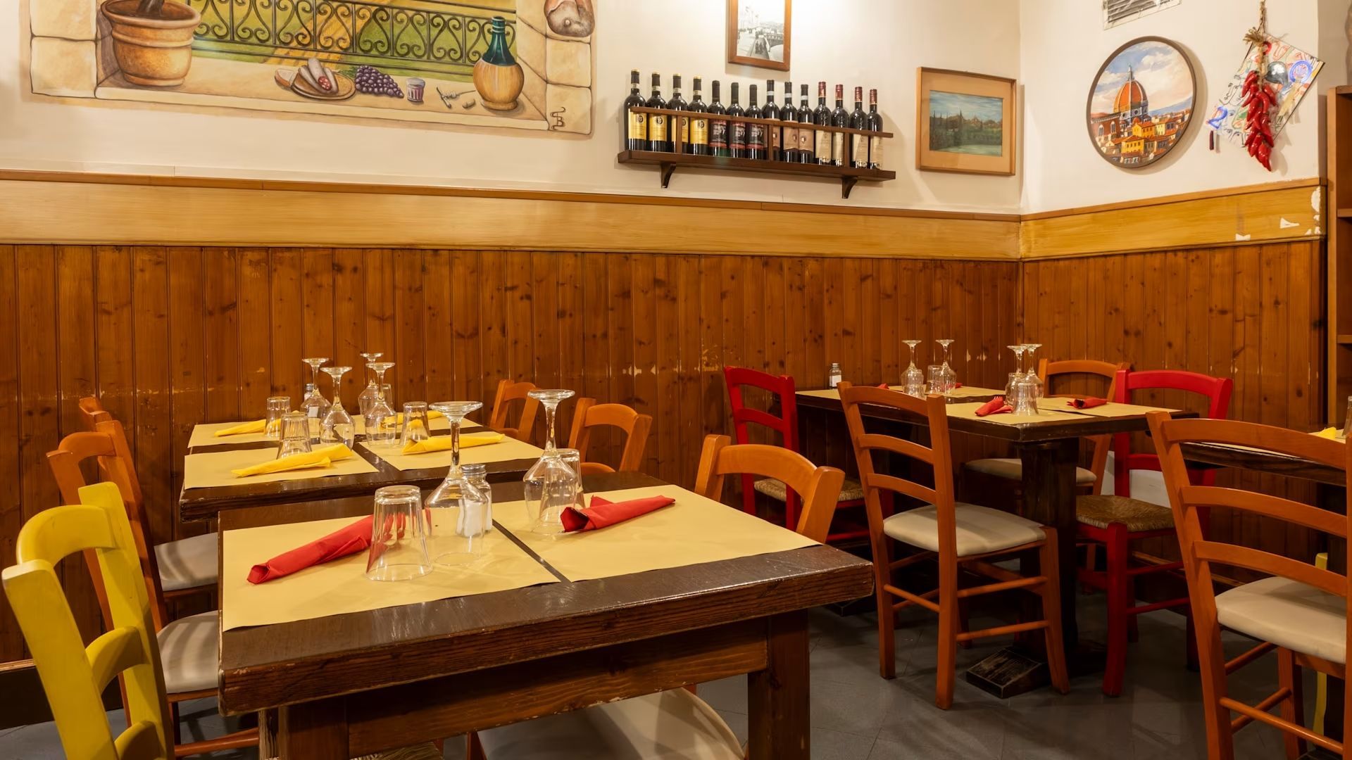Accogliente interno del ristorante con tavoli in legno, sedie rosse e calde decorazioni murali.