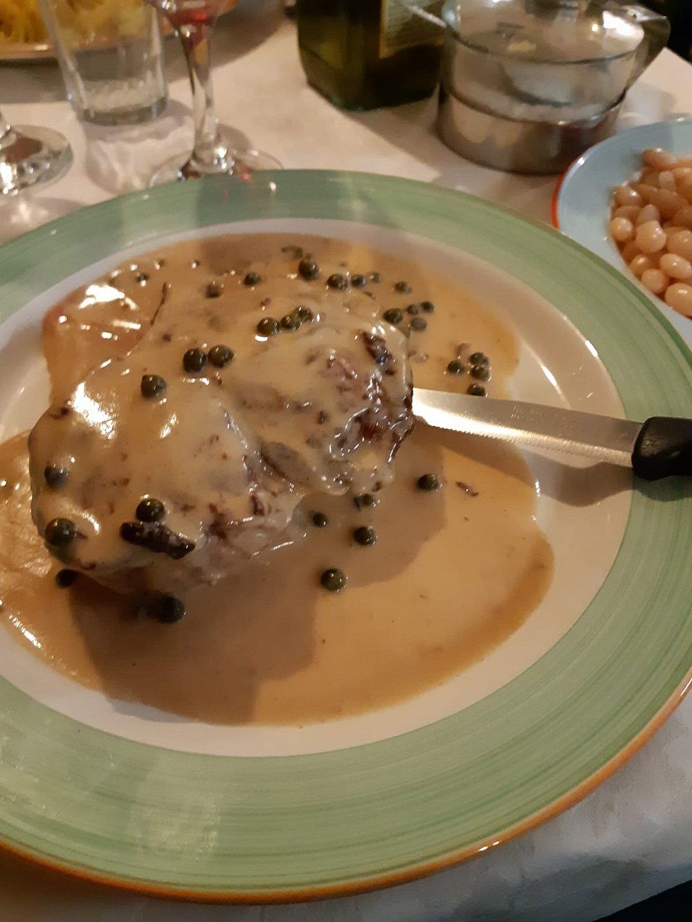 Pollo cremoso ricoperto di funghi su un piatto verde con un cucchiaio a tavola