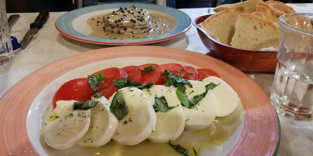 Insalata Caprese con pomodori, mozzarella, basilico e olive servita su un tavolo da pranzo con pane e acqua.