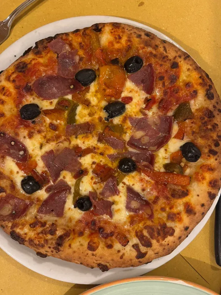 Pizza con peperoni e olive su un piatto bianco sopra una tovaglia gialla.
