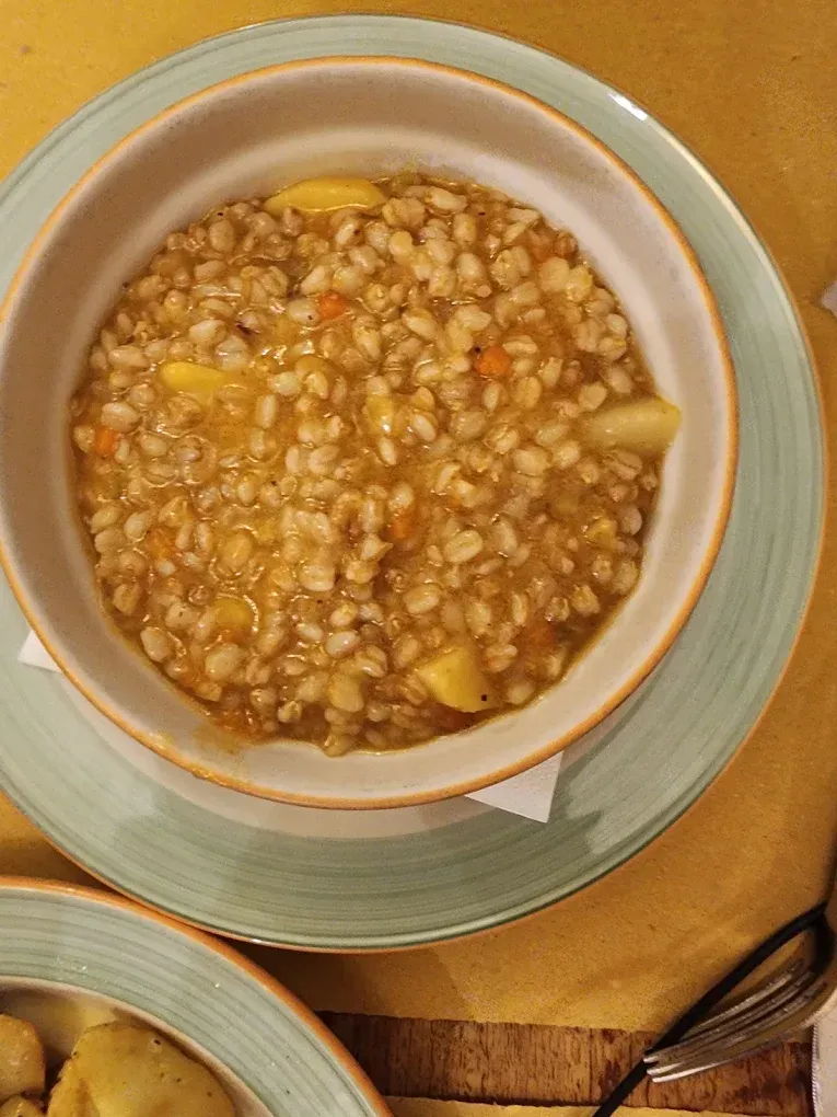 Una ciotola di zuppa sostanziosa con fagioli e pezzi di patate su un piatto verde chiaro, con un cucchiaio a portata di mano.