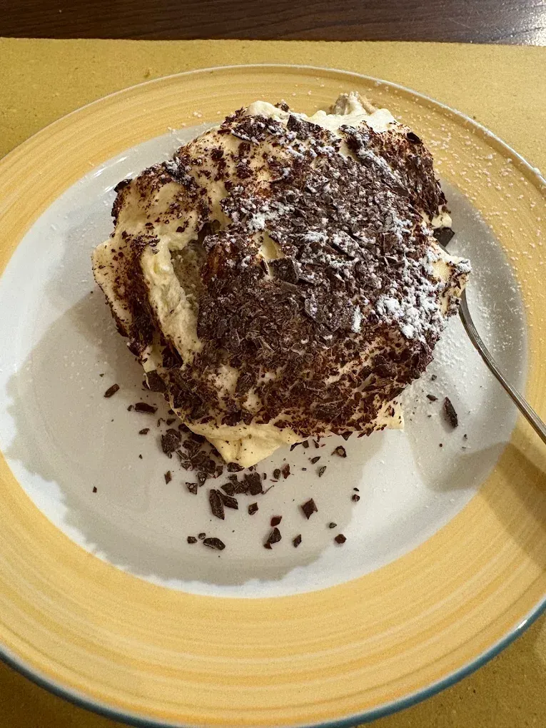 Dessert al cioccolato con cacao e panna su un piatto bianco con bordo giallo.