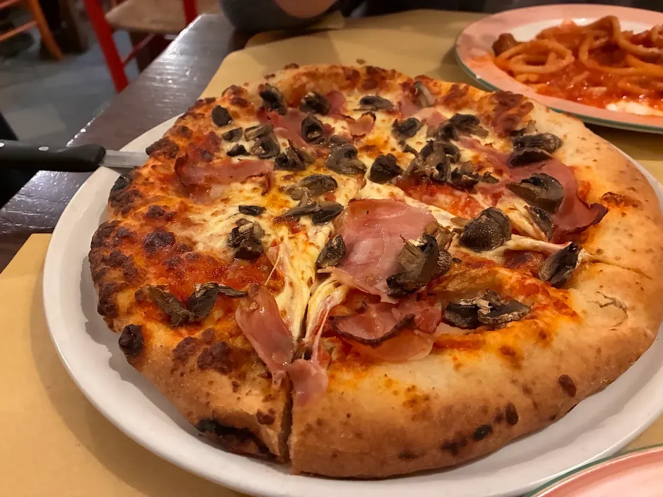 Primo piano di una pizza con peperoni e funghi su un piatto bianco, con patatine fritte sullo sfondo.