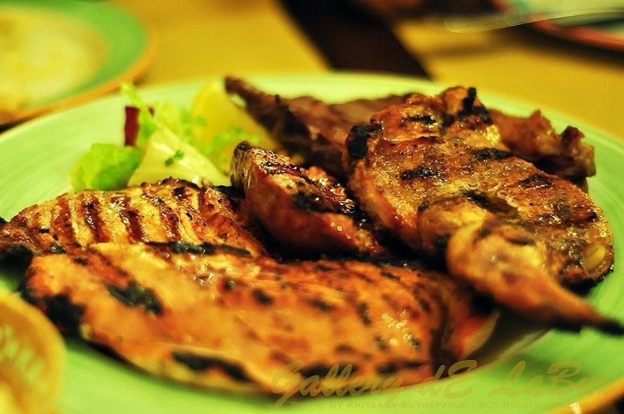 Pezzi di pollo grigliato su un piatto verde con guarnizione di lattuga e un contorno sullo sfondo.