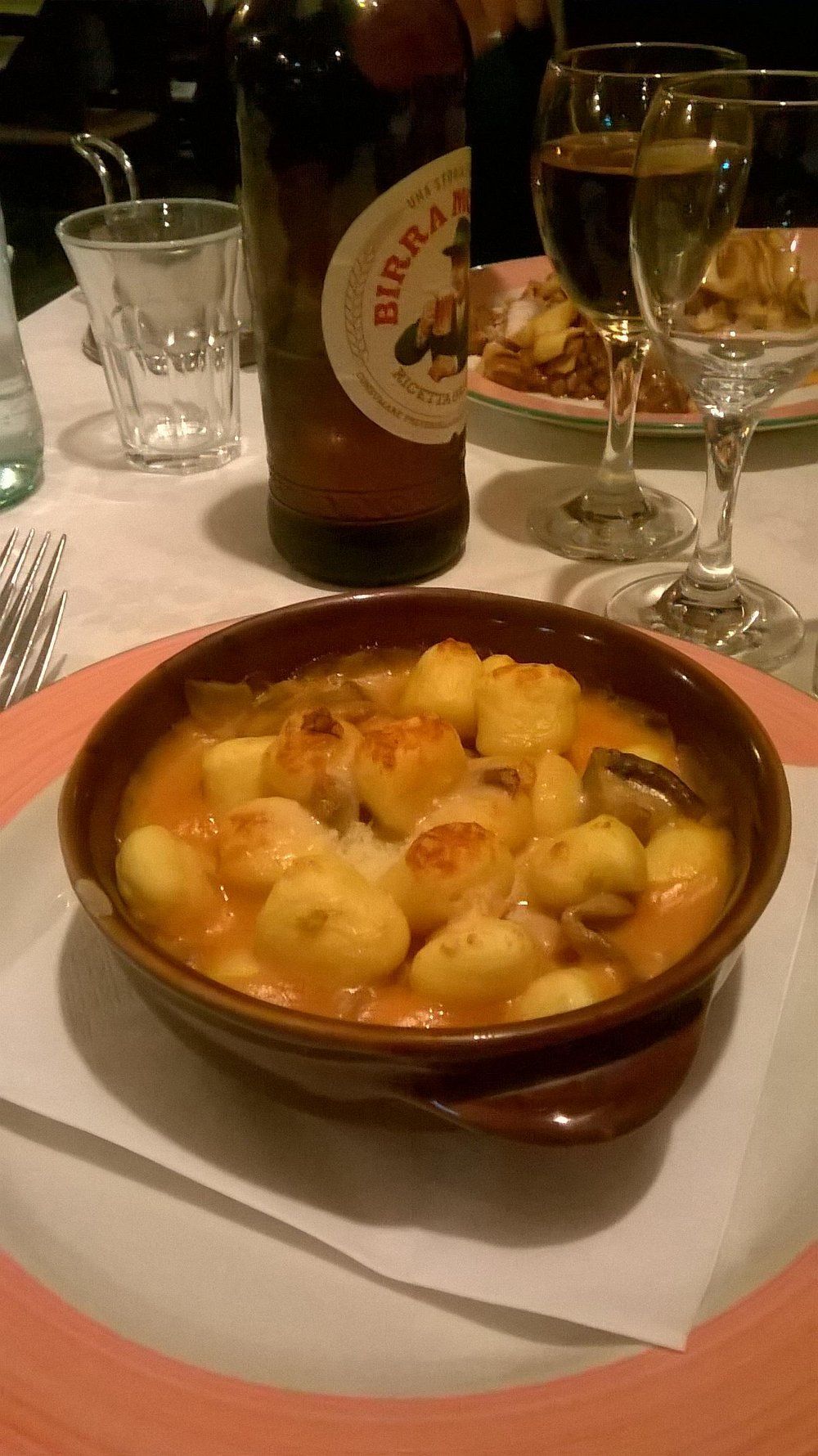 Una ciotola di antipasto a base di frutti di mare al forno su un tavolo del ristorante, con bicchieri di birra e vino nelle vicinanze.