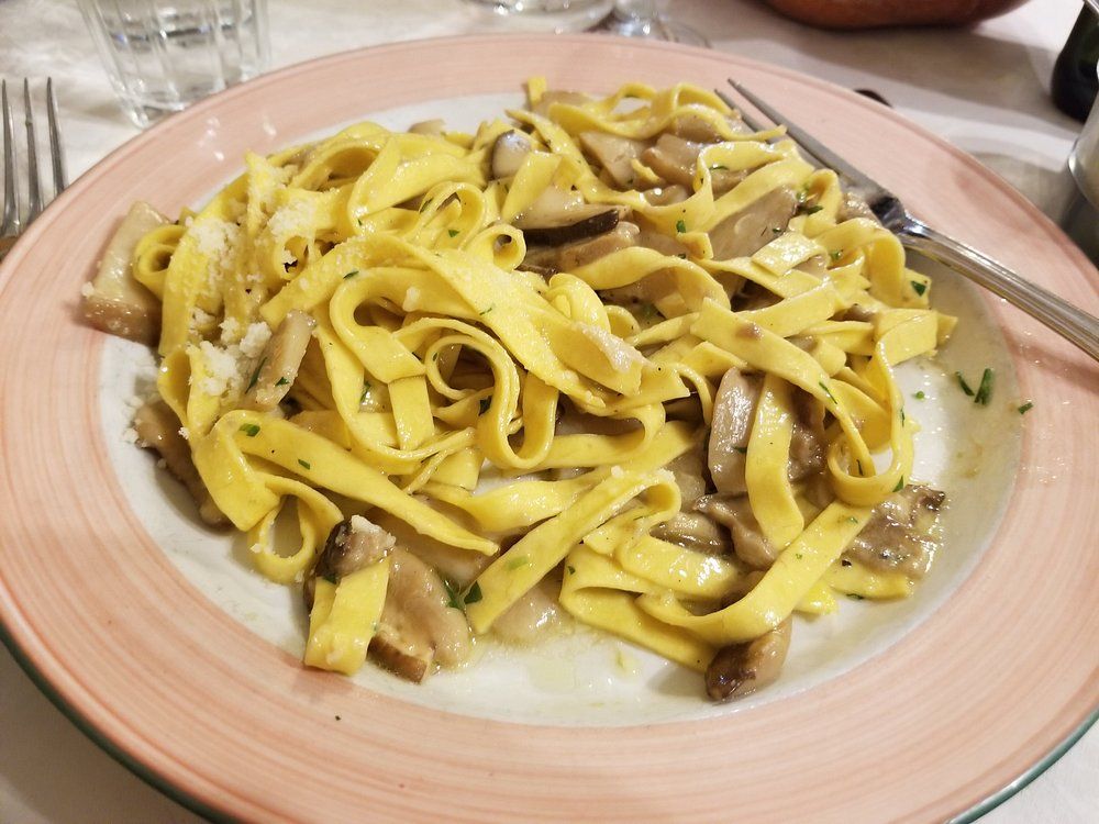 Piatto di tagliatelle gialle con funghi in salsa cremosa su un piatto rosa