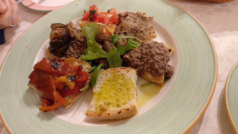 Antipasto in stile mediterraneo con carne alla griglia, verdure arrosto e pane, servito su un tavolo di ristorante.