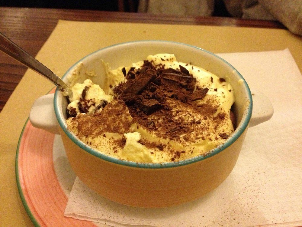 Ciotola di dessert guarnita con cacao in polvere e panna montata, con un cucchiaio su una tovaglietta.
