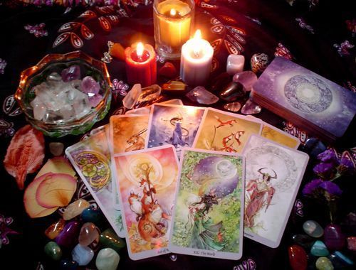 Tarot cards fanned out on a dark cloth, lit by candles and surrounded by crystals and flowers.