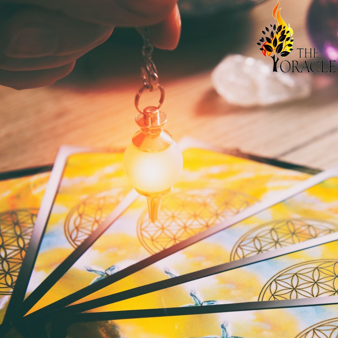 Hand holding glowing pendulum over tarot cards with floral patterns, warm lighting.
