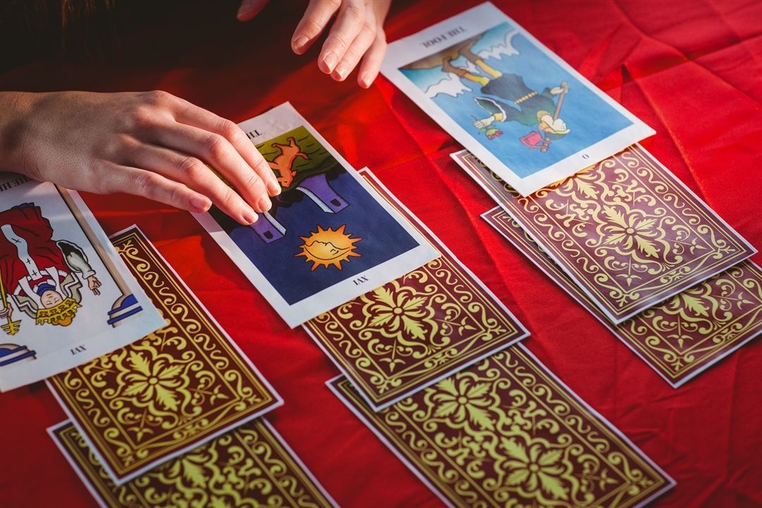 Hands arranging tarot cards on a red cloth. Cards show illustrations, some face-up.
