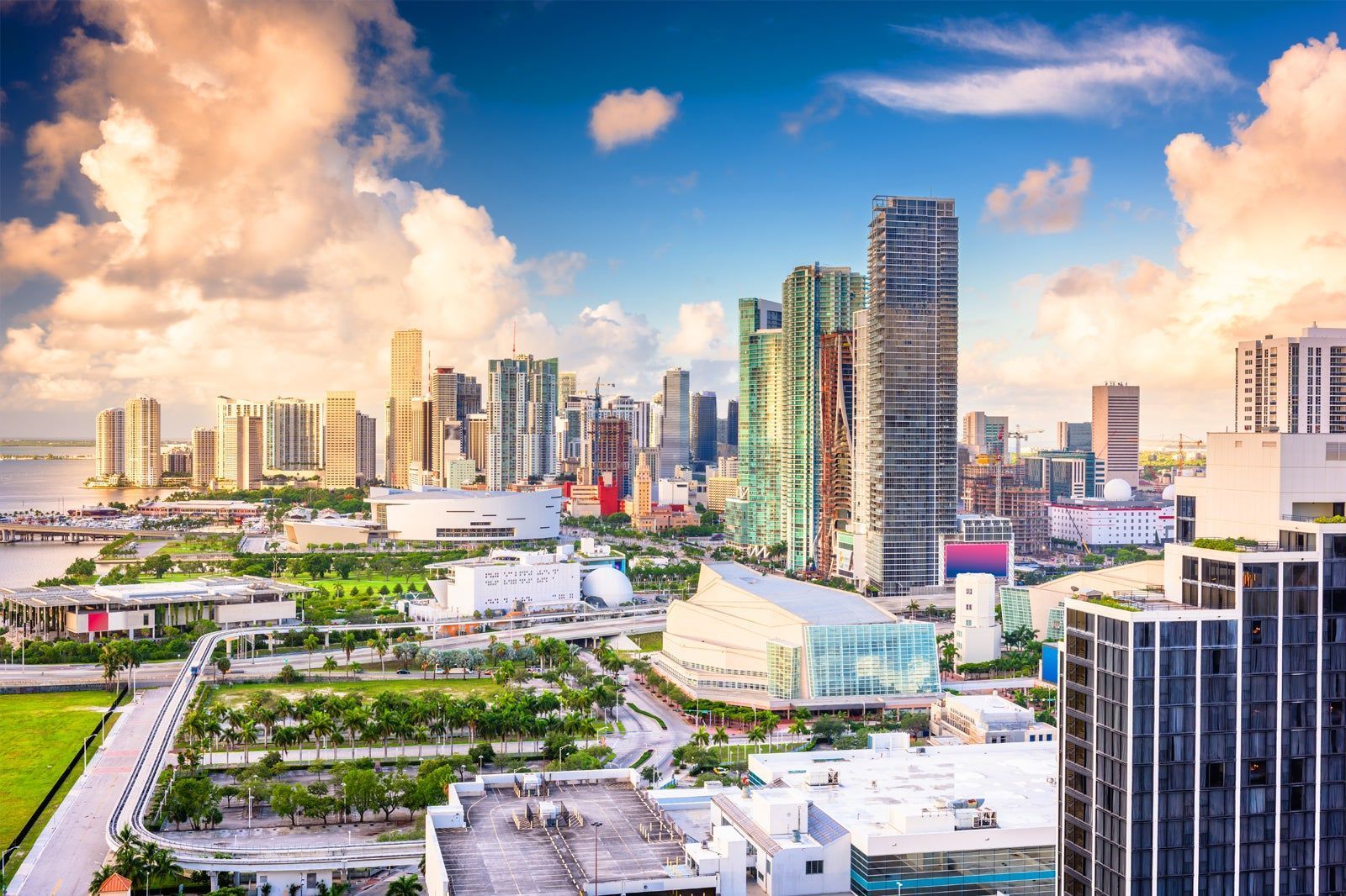 Downtown Miami skyline with skyscrapers under a partly cloudy sky, featuring buildings and green spaces.
