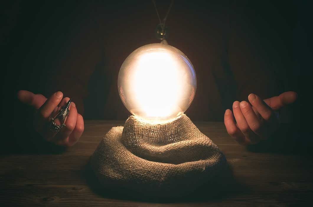 Glowing crystal ball on a burlap-covered base, with hands on either side, indoors.