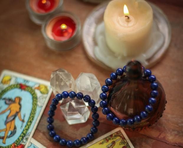 Tarot cards, candles, crystals, and blue bead bracelets on a wooden surface.