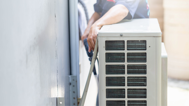 A man is installing an air conditioner on the side of a building.