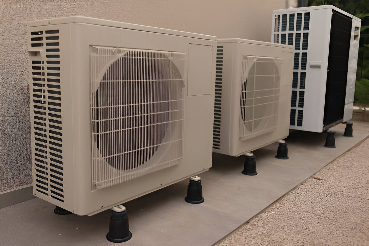 Three air conditioners are lined up on the side of a building.