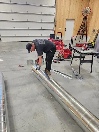 A man is working on a metal pipe in a garage.