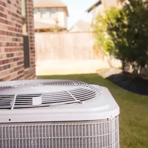 An air conditioner is sitting in the backyard of a brick house.