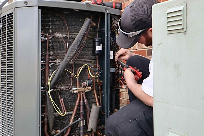 A man is working on an air conditioner outside of a building.
