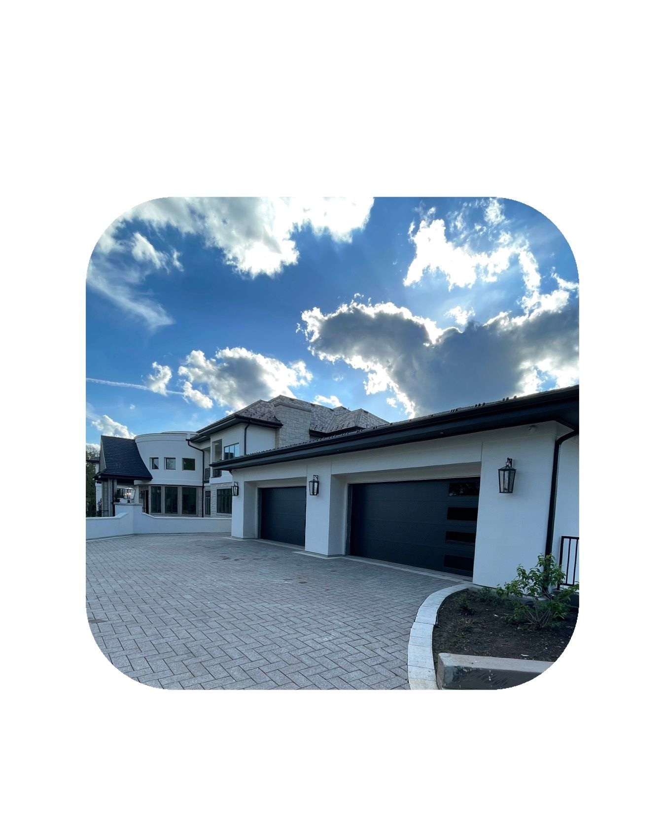 Modern white house with dark garage doors, blue sky, and brick driveway.