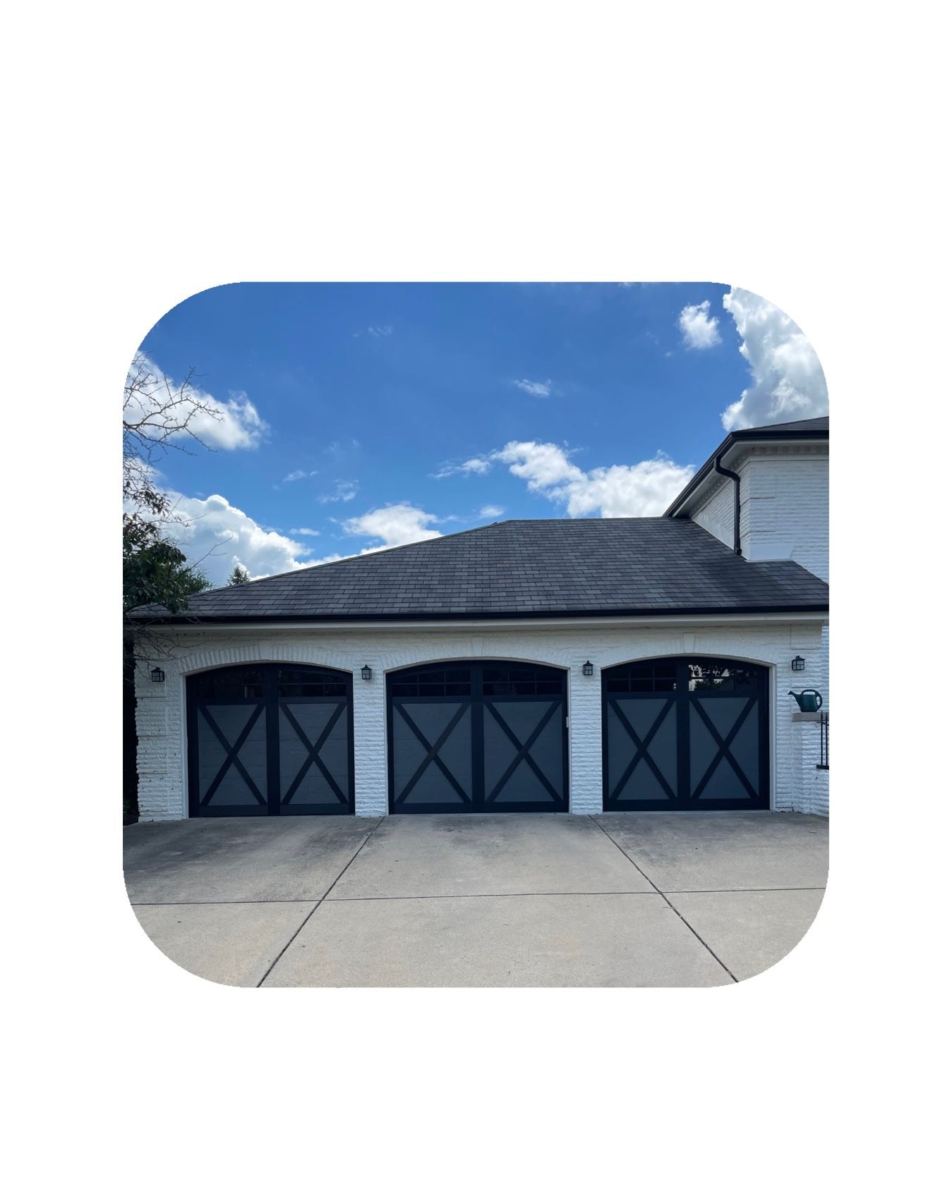Three-car garage with black doors and gray roof, under a bright blue sky with clouds.