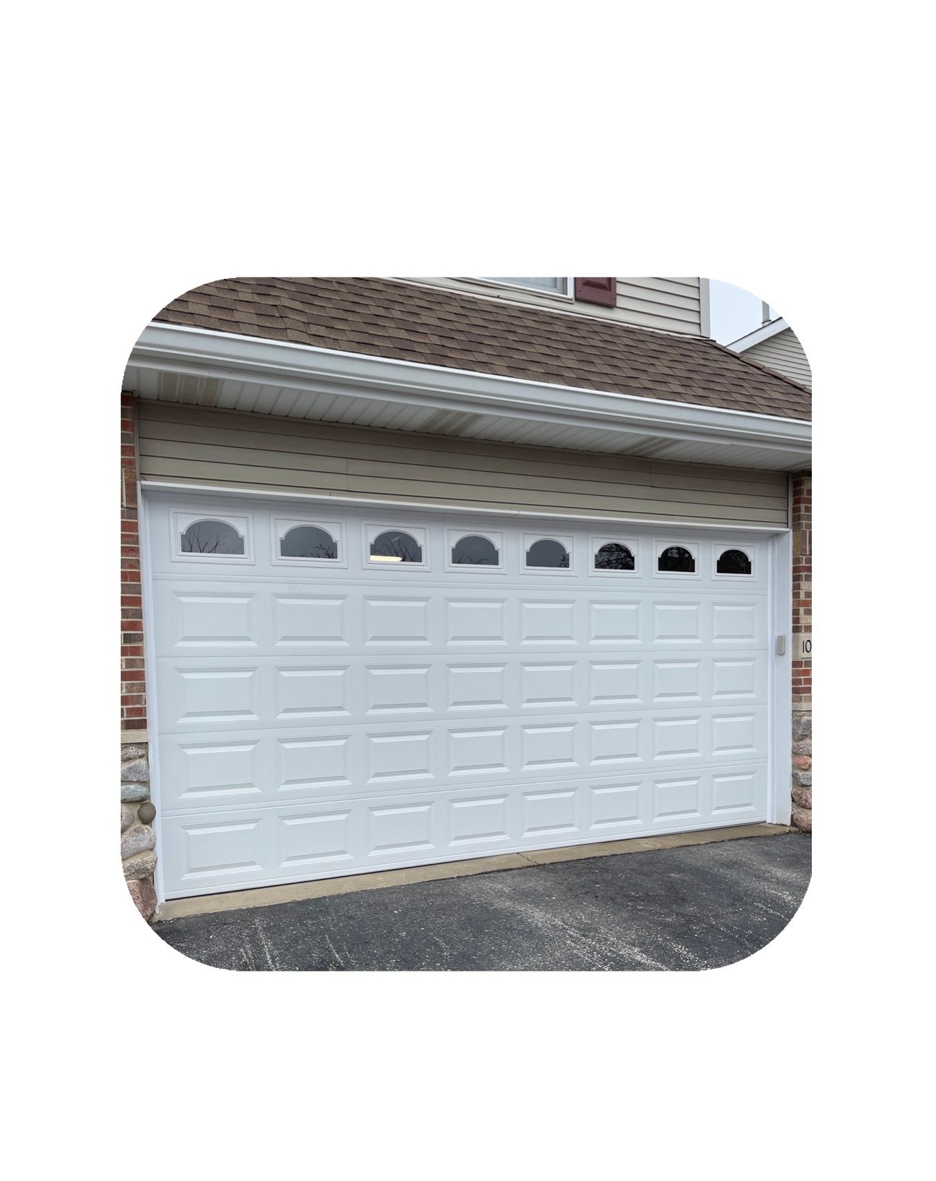 White garage door with arched windows; brick and shingle house exterior.