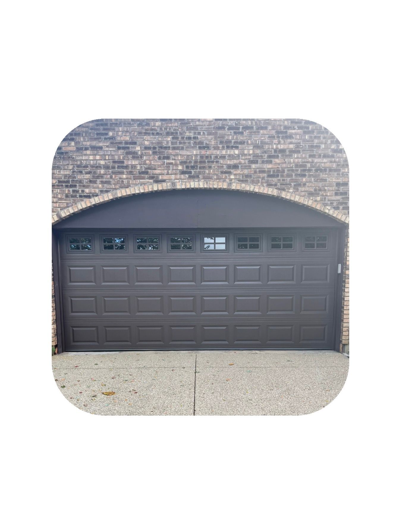 Brown garage door with windows, set in brick archway, on a gravel driveway.