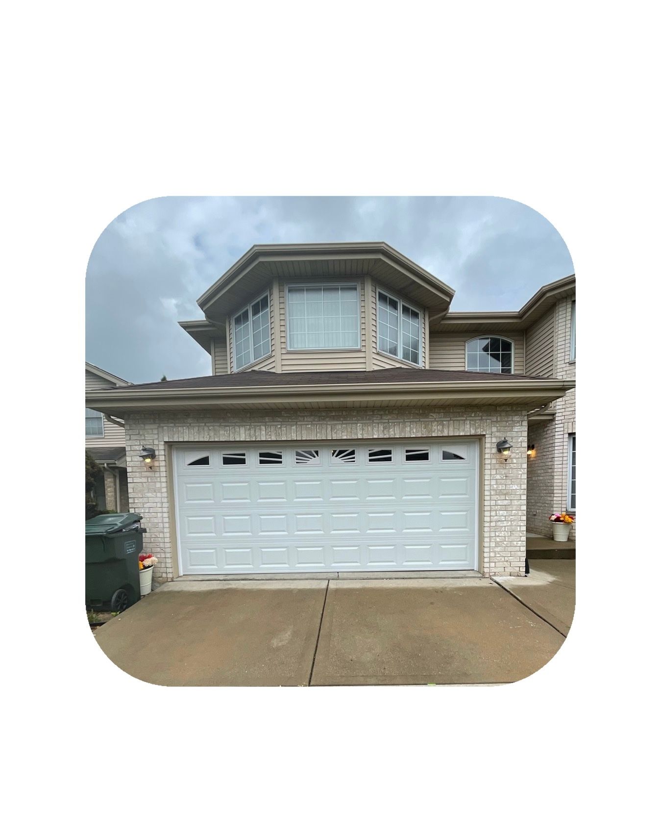 White garage door on a brick house with a second-story bay window. Overcast sky.