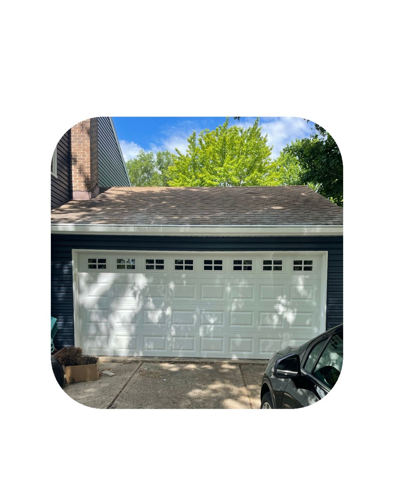 White garage door with windows, blue siding, brick chimney, and a car parked in front.