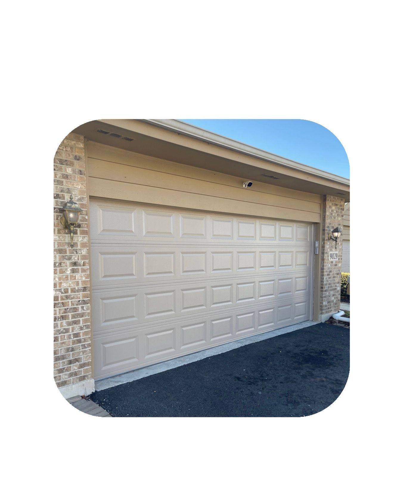 Beige garage door on a brick building with asphalt driveway.
