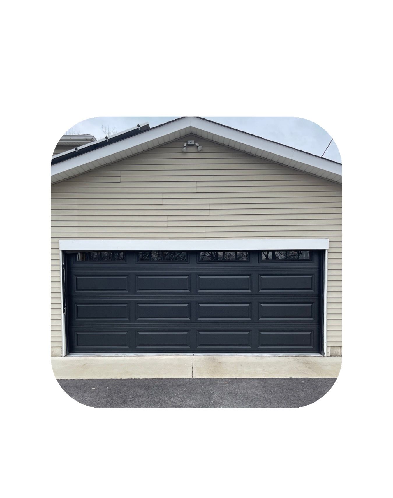 Dark gray garage door on a beige house, with a dark asphalt driveway.