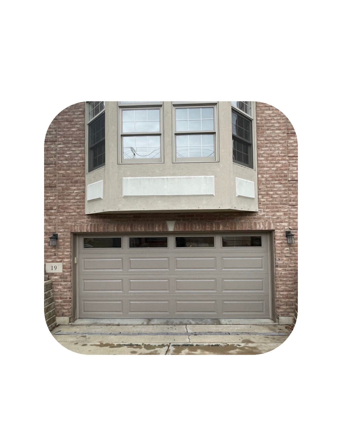 Tan garage door under a bay window with brick exterior.